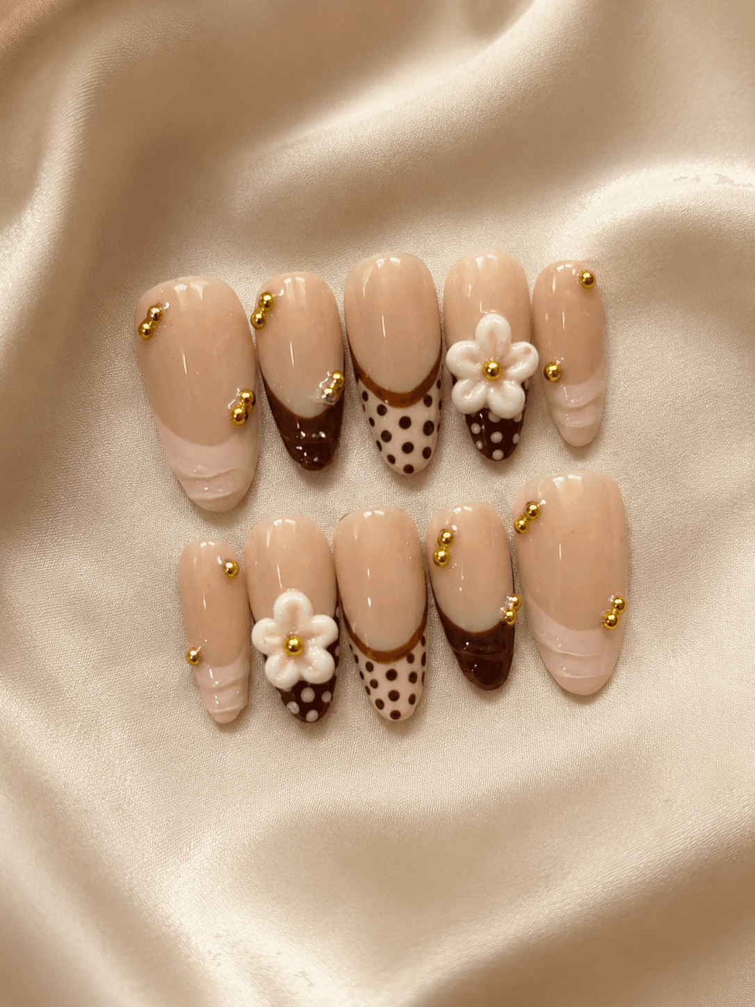 Coquette florals — Nude nails dressed up with chocolate drips, polka dots, 3D florals, and gold pearls