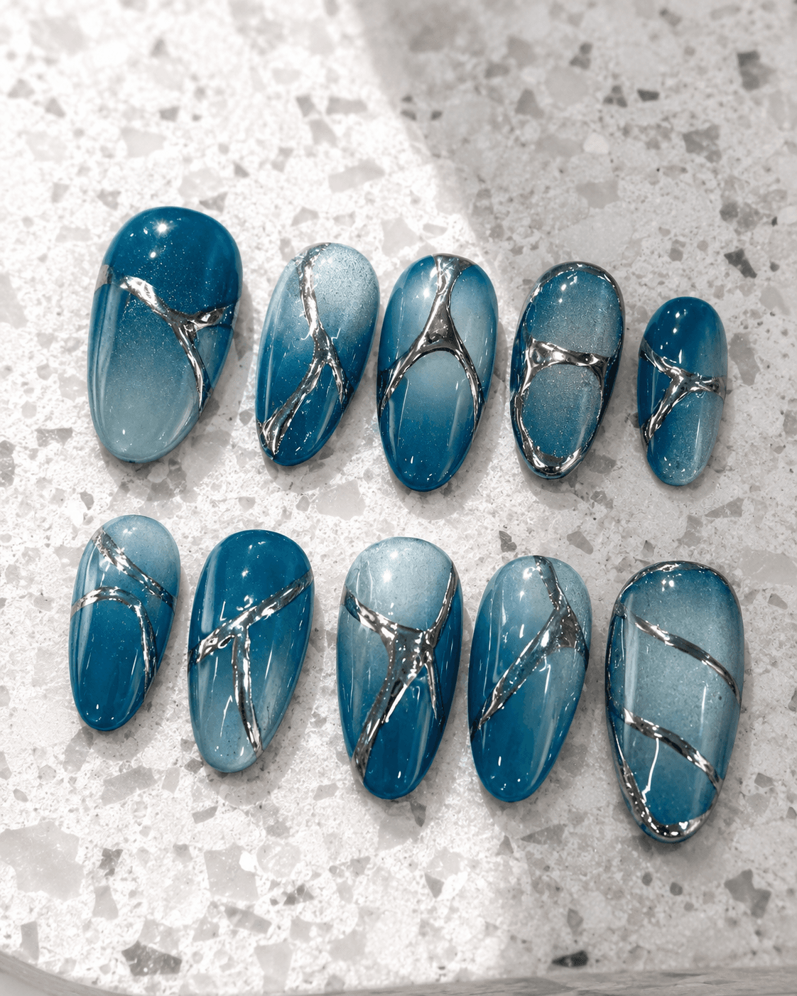 Cracked Ice — Ocean-blue ombré almond nails with metallic chrome crack details.
