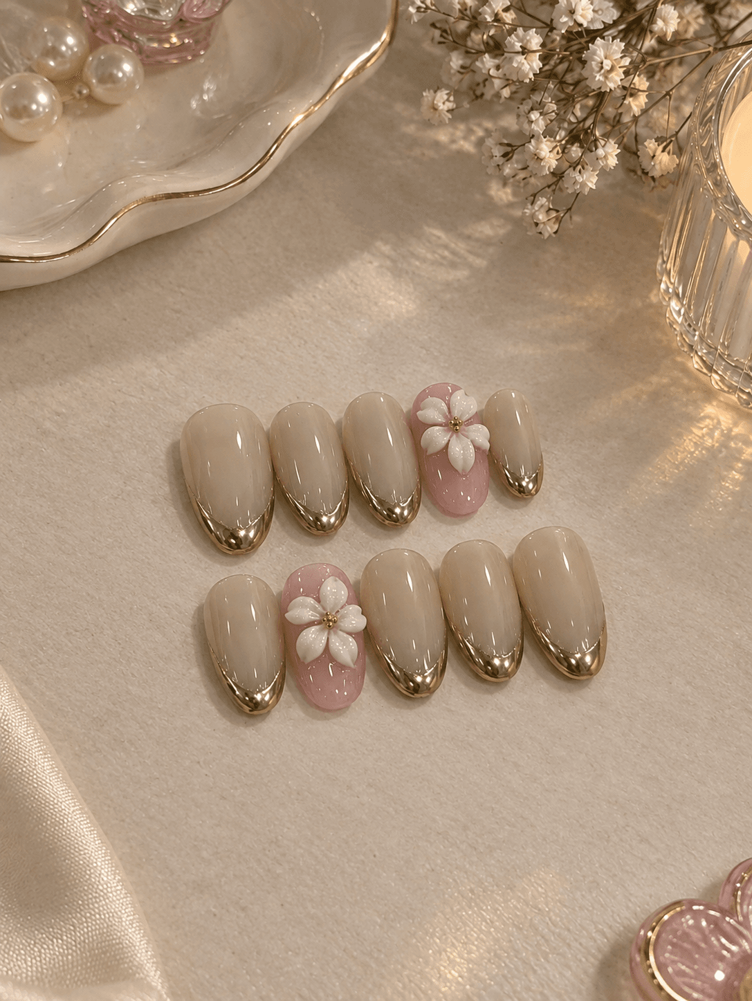 Golden Blossom — Creamy nude almond nails with gold chrome French tips and a 3D white flower on pink accent nails.